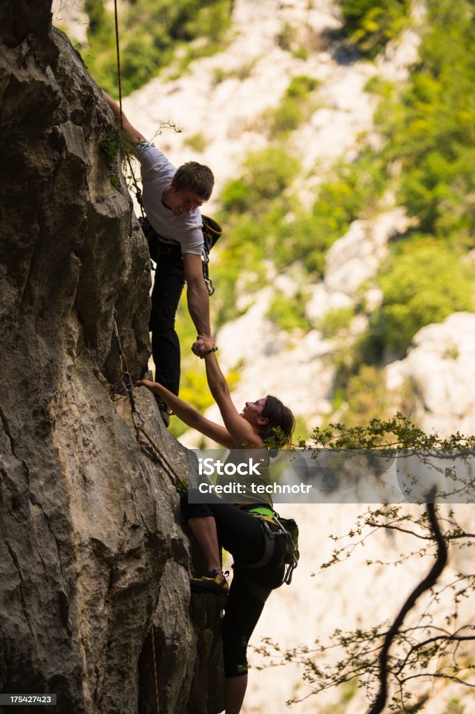 Giovane coppia di arrampicata aiutando a vicenda nel muro di pietra - Foto stock royalty-free di Alpinismo
