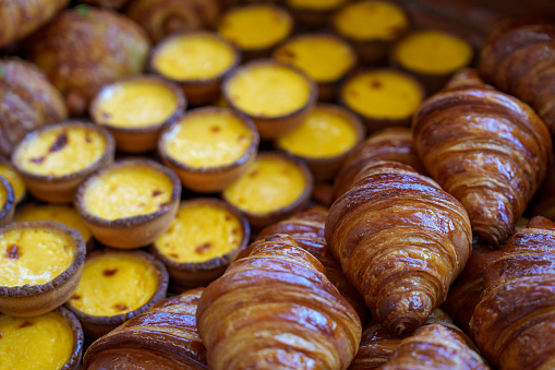 Various freshly baked pastries, including egg tarts and croissants, for sale in a bakery store