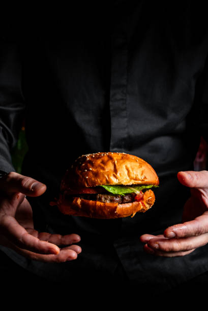 istock chef man in a black uniform throwing burger on black background. 1754276709