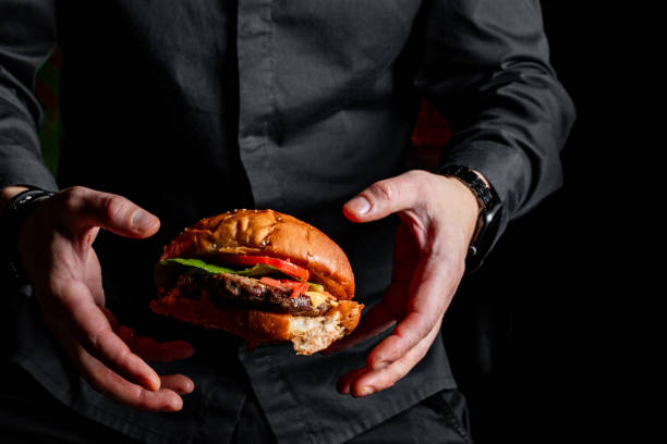 chef man in a black uniform throwing burger on black background.