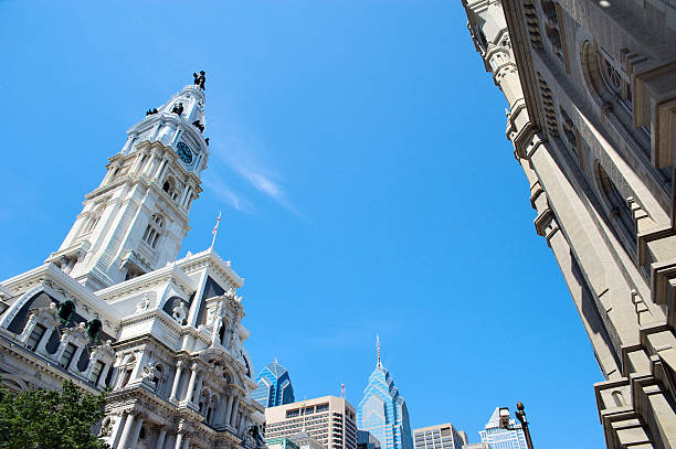 Philadelphia City Hall tower points towards the blue sky. On the foreground several historic buildings. On the background modern skyscrapers.