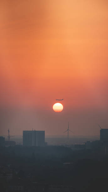 istock Passing plane over Amsterdam dives into the solar disc during sunset. Travelling in modern times. City immersed in smog and an orange sky 1754279478