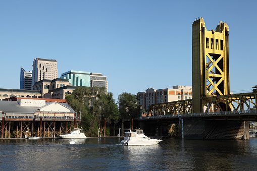 Boats traveling on the Sacramento River along the downtown skyline. The Tower Bridge links West Sacramento in Yolo County to the west. Sacramento is the capital city of the U.S. state of California