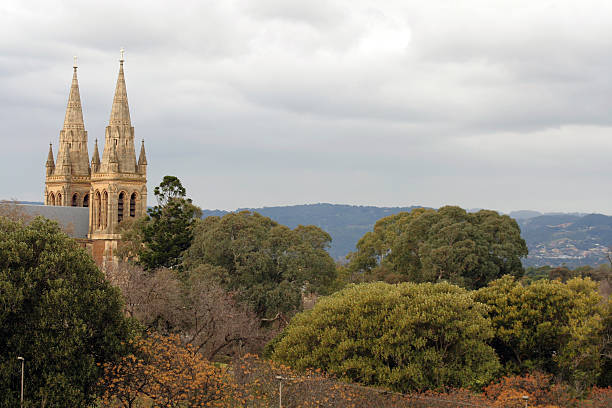 The twin spires of a cathedral in a sea of autumn trees against a cloudy sky.