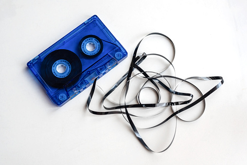 Closeup of an old blue audio cassette tape with the magnetic tape sticking out and tangled on white background. Apsolete technology