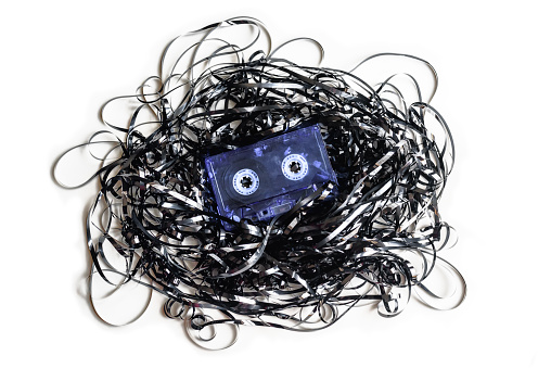 Old audio cassette tape with all the magnetic tape out and tangled on white background. Apsolete technology