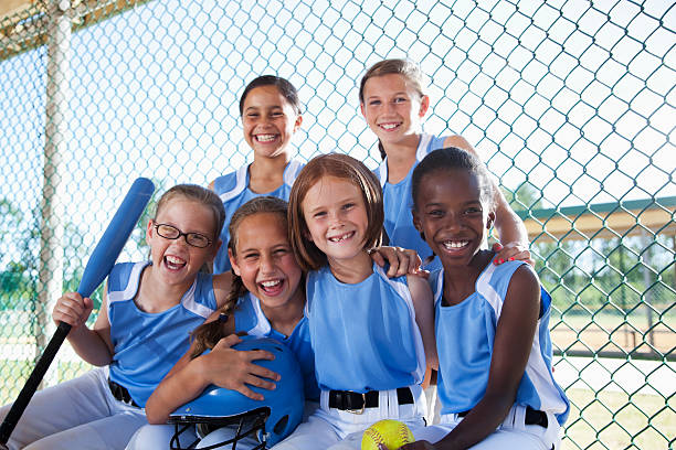 niñas de softball equipo de estar en el banquillo de campo de béisbol - team sport enjoyment horizontal looking at camera fotografías e imágenes de stock