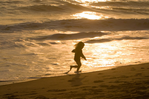 A silhouette of a young girl running on the beach.