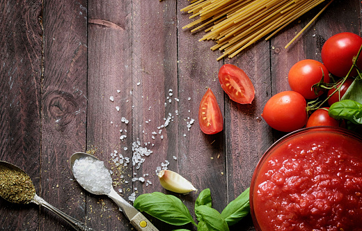 Italian food. Homemade tomato sauce, basil, whole wheat pasta, garlic and spices on rustic wooden background. Ingredients for cooking tomato pasta. Overhead view.