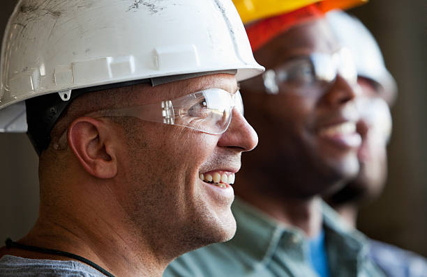 Close up group of construction workers Close up of group of multi-ethnic construction workers wearing hard hats and safety glasses.  Focus on man in foreground (30s). blue collar worker stock pictures, royalty-free photos & images