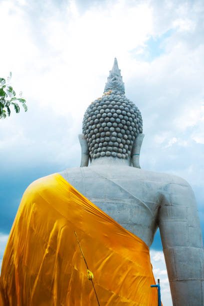 Back o f large thai buddha statue on and between rocks and trees high up  on  grounds of rural small village Parangmee in district Noen Maprang in province of Phitsanulok in Thailand.