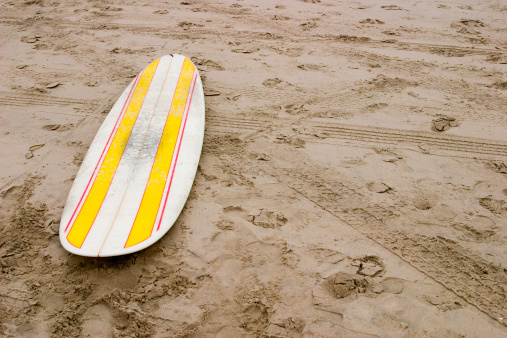 A LONGBOARD SITS IN THE SAND.