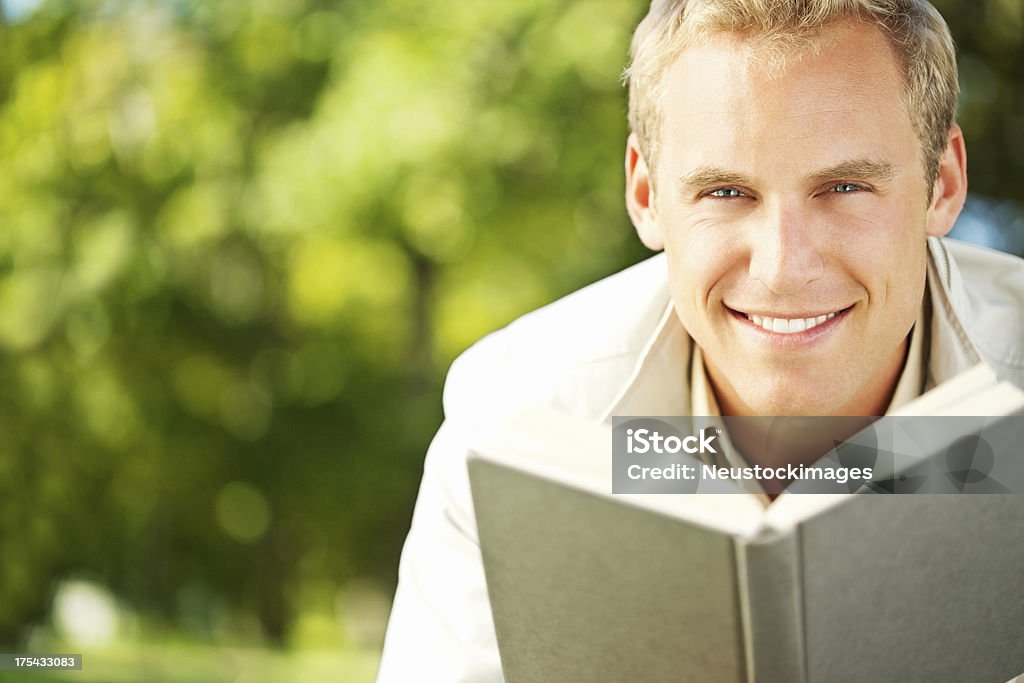 Smiling Young Man Reading a Book Portrait of a smiling young man reading a book. Horizontal shot. Adult Stock Photo