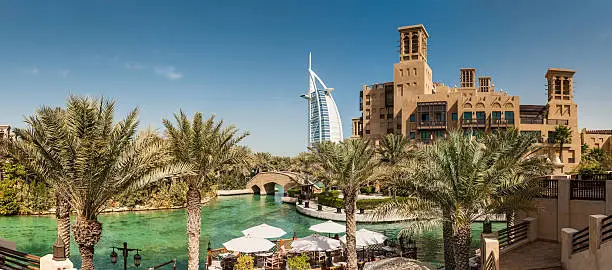 "The iconic futuristic sails of the luxury Burj Al Arab hotel towering over the traditional wind towers and tranquil palm fringed oasis of the Madinat Jumeirah on the coast of Dubai, United Arab Emirates. ProPhoto RGB profile for maximum color fidelity and gamut."