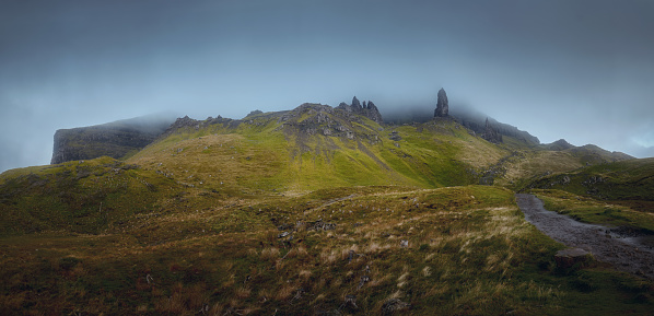 Atmospheric panorama of high sharp cliffs, the path leading to the top and the looming rain cloud. The Storr, The Isle of Skye, Scotland, UK