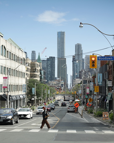 Toronto, Canada - August 27, 2023: A pedestrian crosses the 1200-block of Yonge Street at Woodlawn Avenue. The Rosedale neighbourhood includes upscale shopping and dining in the Midtown area. Traffic goes under an elevated railway bridge. Tall office and residential towers stand near Yonge at Bloor Street. Summer afternoon.