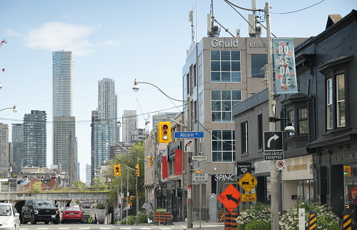 Toronto, Canada - August 27, 2023: Looking south on Yonge Street in the Rosedale area lined with upscale shops and restaurants. Traffic passes under the railway bridge. Tall office and residential towers stand near Bloor Street in the background. Summer afternoon with blue skies.