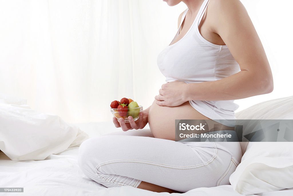 Pregnant young woman holding fruit bowl Pregnant young woman holding fruit bowl - sitting on bed 20-29 Years Stock Photo