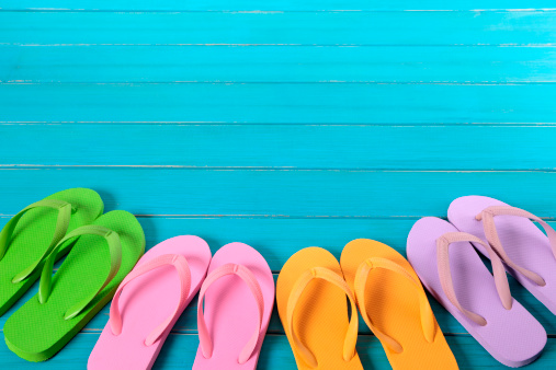Row of colorful flip flops on old weathered blue painted beach decking.  Space for copy.   Alternative version shown below: