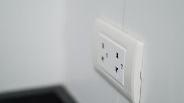 Hand holding electric plug and smartphone charger put on multiple socket on the wall. Electrical wires and power strips. Save energy electrical concept.