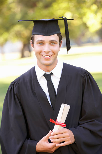 Male Student Attending Graduation Ceremony Male Student Attending Graduation Ceremony Holding Diploma Smiling At Camera graduation photos stock pictures, royalty-free photos & images
