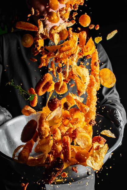 Closeup of chef throwing snack mix from bowl on black background.