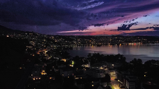 Here is a shot in the city of Bäch in Switzerland at sunset near the lake. The lights of the city create a beautiful and visible coastline. This picture was shot at about 8 pm (20:00) by a drone.￼