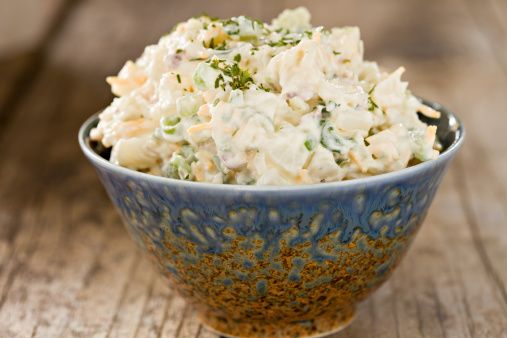 An extreme close up shot of a fancy blue bowl full of freshly made creamy potato salad. Shot on an old wooden background.