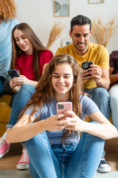 istock Group of young people sitting on sofa and using mobile phones at home 1754387776