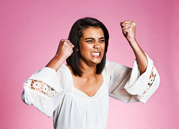 Beautiful young woman shakes her fists and grimaces in rage This beautiful young Indian woman with her eyes screwed up and shaking her clenched fists has totally lost her temper. All against a rose pink background. clenching teeth stock pictures, royalty-free photos & images