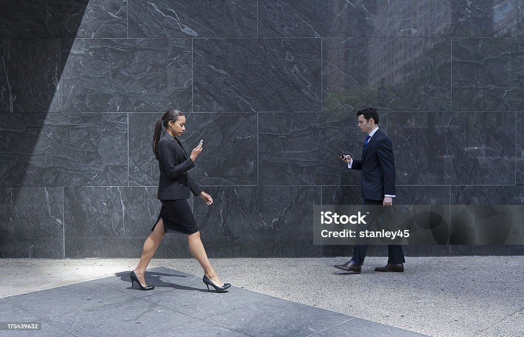 Pareja de negocios con los teléfonos celulares caminar sobre la acera a la ciudad - Foto de stock de 20 a 29 años libre de derechos