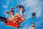 Two electricians from cradle of aerial platform or crane are repairing street lighting lamp.