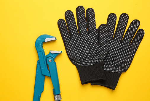 Adjustable wrench and work gloves on yellow background. Plumbing work. Flat lay