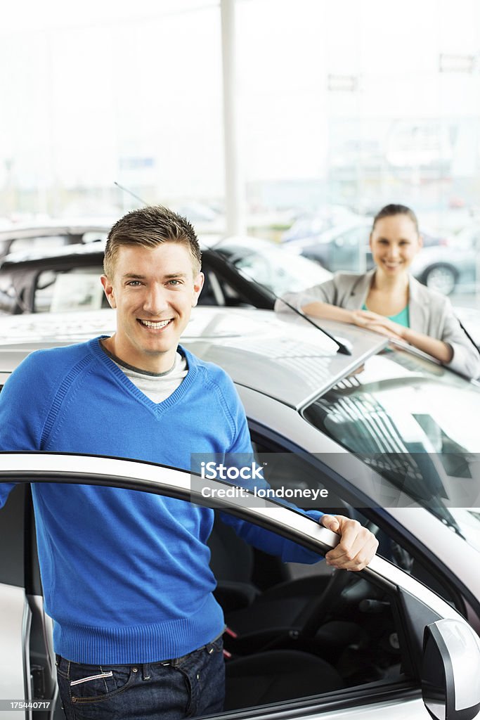 Happy Young Couple By New Car Portrait of a young man with girlfriend standing by new car at showroom. Vertical shot. Car Stock Photo