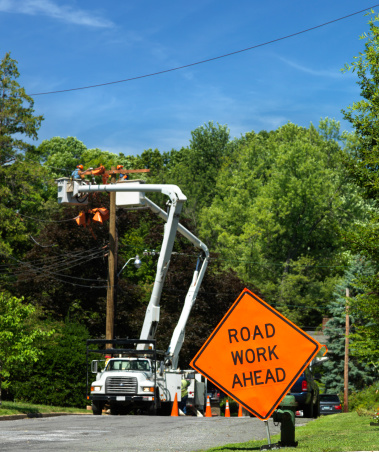 Focus on Road Work Ahead traffic sign with electric power utility trucks in background.See other Road work signs in my LOCATIONS Lightbox.