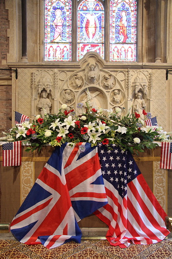 Altar in a church decorated with Union Jack and Stars and Stripes flags. A huge display of white lilies and red poppies sit on altar