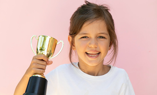 Little girl raising a winning glass one hand, on pink background.