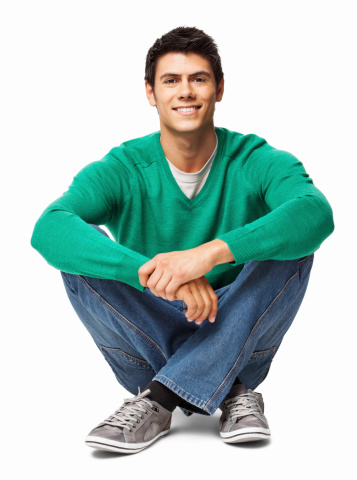 Portrait of a relaxed young man in casual wear sitting on floor. Vertical shot. Isolated on white.