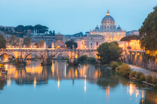 Scenic twilight view of Saint Peter's Basilica at Vatican City and Ponte Vittorio Emanuele II illuminated along the Tiber River on a summer evening in Rome, Italy.