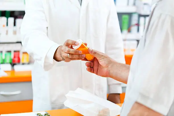 Photo of Pharmacist giving pill bottle to customer at hte pharmacy