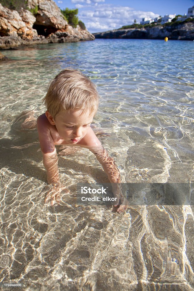 Piccolo ragazzo alla ricerca di conchiglie in acqua alla spiaggia di sabbia. - Foto stock royalty-free di 2-3 anni