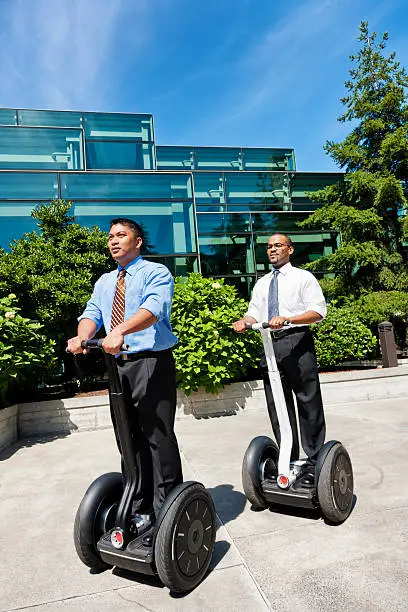 Photo of two businessmen commuting on Segway personal transport devices.