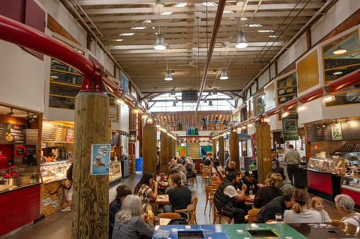 Communal eating area (food hall) in Granville Island Public Market, on Granville Island, Vancouver, Canada. Customers can each buy food at which ever food outlet they choose, then sit together.