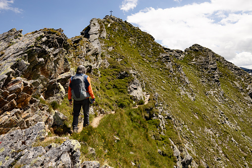 Man with backpack climbing steep rocky trail up to summit marked with cross, Austria. High quality photo