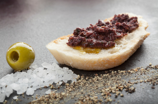 Ciabatta bread with olive tapenade and salt and pepper in foreground.  On a slate platter.