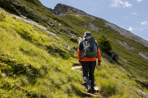 A man with a backpack climbs a steep path to a rock ridge in the Austrian Alps. High quality photo