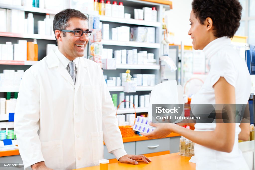 Woman shopping for drugs in the pharmacy Female customer holding paper bag and pills, talking with male pharmacist, shopping for drugs in the pharmacy. Adult Stock Photo