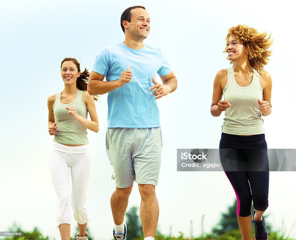 People Jogging Outdoors. Three people, jogging outdoors and having fun. Two women and man enjoy morning sun and exercise outdoors. Selective focus to man. 30-39 Years Stock Photo