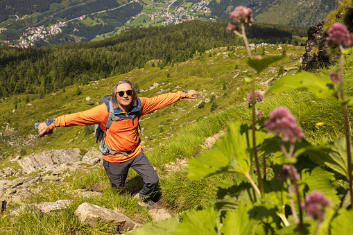 Top view of gray-haired long-haired male traveler with backpack among alpine slopes, Austria. High quality photo