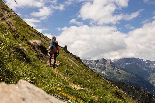 Gray-haired man with backpack climbing steep slope against bright sky and mountain range, Austria. High quality photo